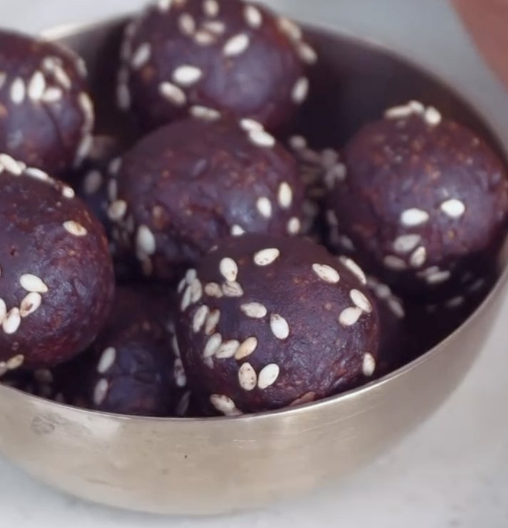Sesame-topped cacao date balls in a brass bowl