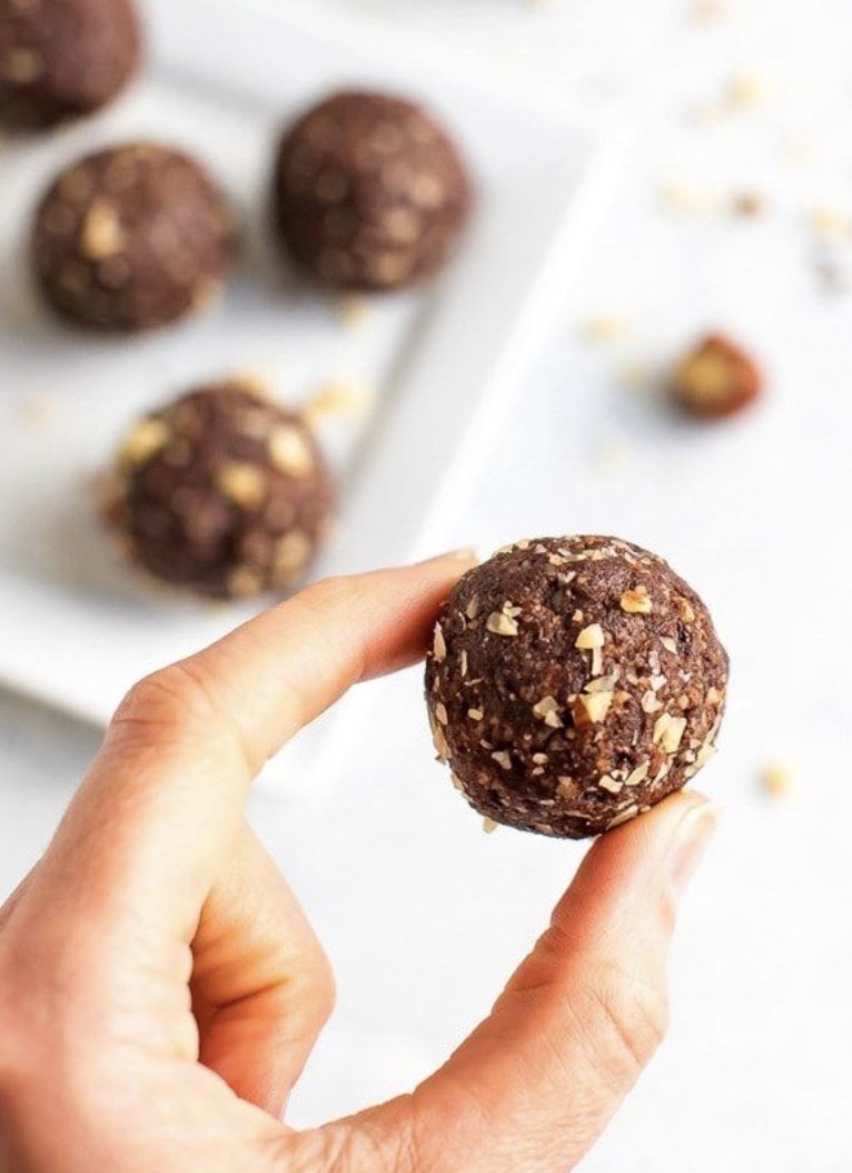 A hand holding a nut-studded cacao energy ball